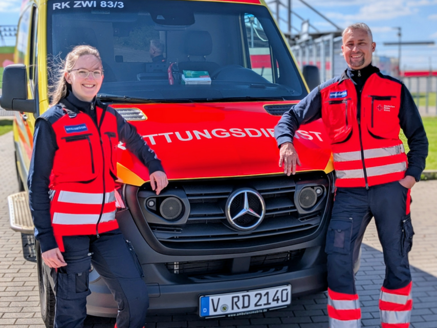 2 Notfallsanitäter stehen in Uniform vor einem Rettungswagen des Deutschen Roten Kreuzes Zwickau