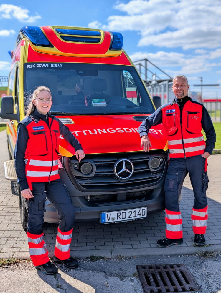 2 Notfallsanitäter stehen in Uniform vor einem Rettungswagen des Deutschen Roten Kreuzes Zwickau