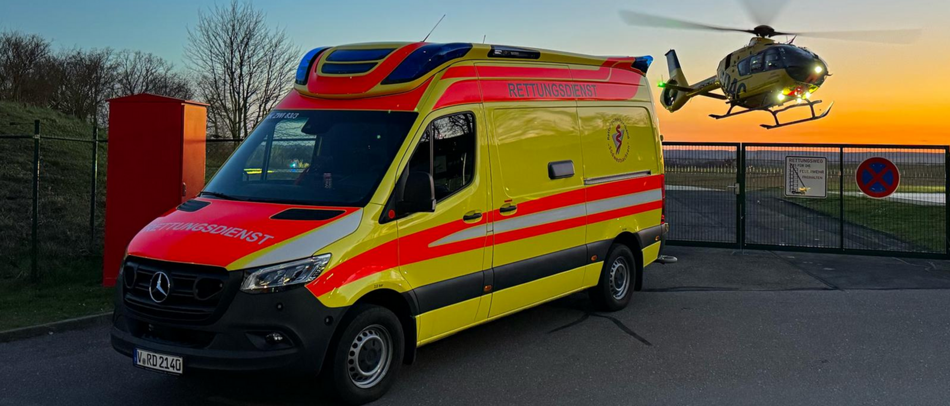 Krankenwagen des Zweckverbandes Südwestsachsen in gelb mit Helikopter des ADAC im Hintergrund