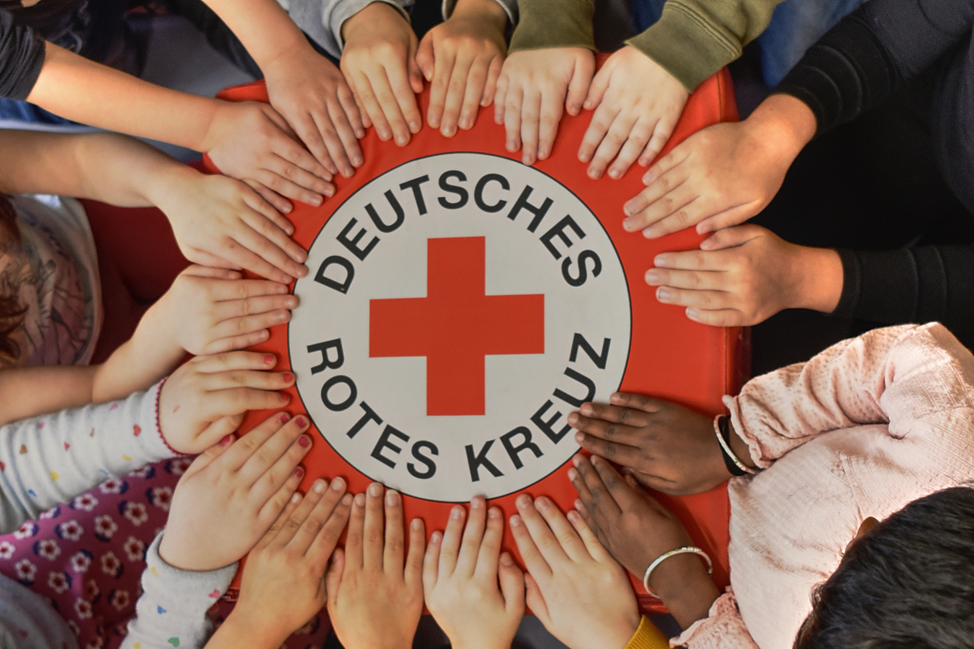 viele Hände umfassen ein Tuch mit der Aufschrift Deutsches Rotes Kreuz